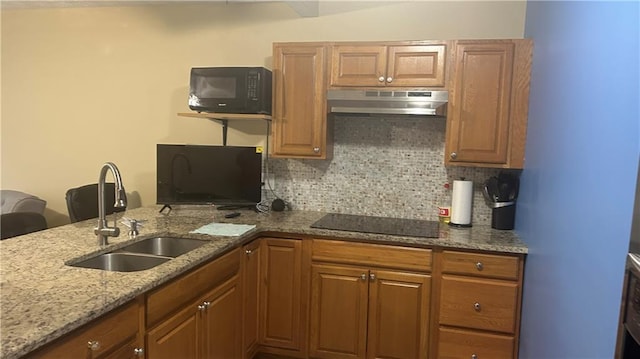 kitchen with under cabinet range hood, black electric cooktop, a sink, tasteful backsplash, and light stone countertops
