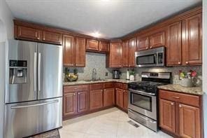 kitchen featuring stainless steel appliances, a sink, light countertops, tasteful backsplash, and light tile patterned floors