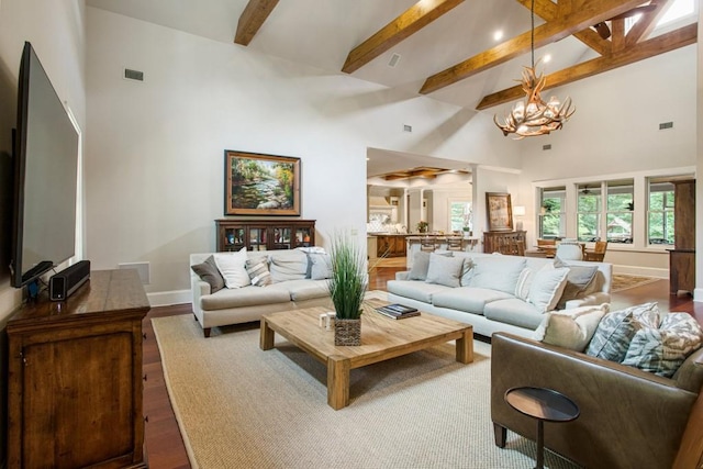 living room with an inviting chandelier, a towering ceiling, beam ceiling, and hardwood / wood-style floors