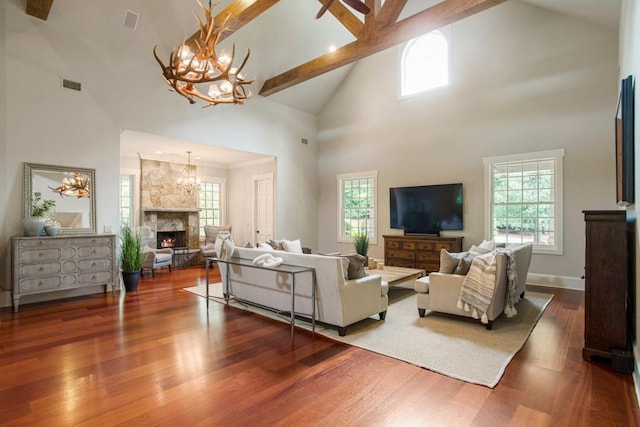 living room featuring a stone fireplace, hardwood / wood-style floors, high vaulted ceiling, beamed ceiling, and a notable chandelier