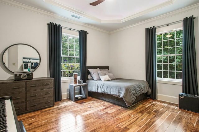 bedroom with crown molding, a tray ceiling, and light wood-type flooring