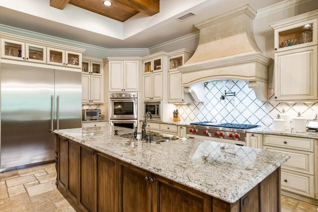 kitchen with built in appliances, sink, cream cabinets, and custom range hood