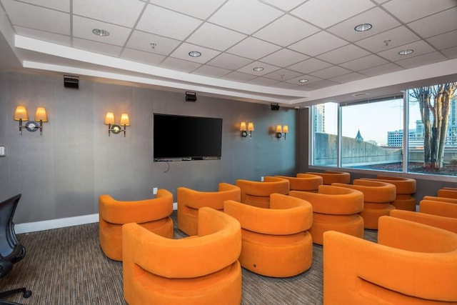 carpeted home theater room featuring a drop ceiling and baseboards