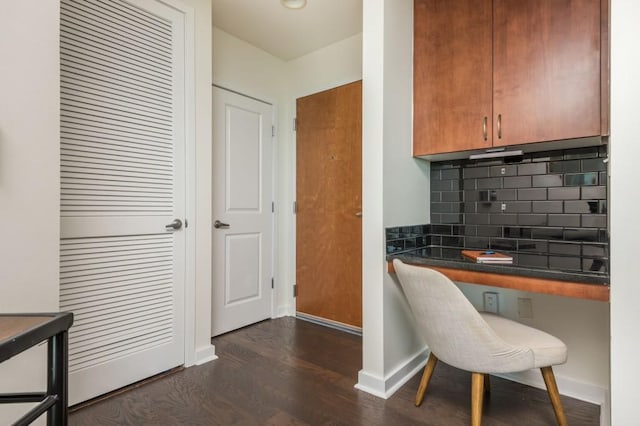 kitchen with dark countertops, dark wood-type flooring, baseboards, decorative backsplash, and built in study area