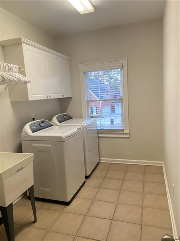 clothes washing area with light tile patterned floors, washing machine and dryer, and cabinets