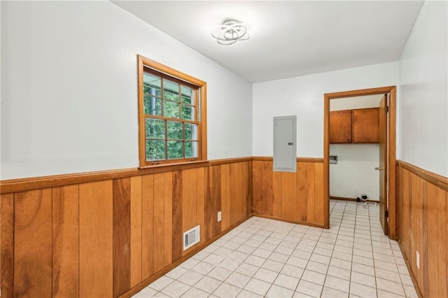 spare room featuring light tile patterned floors, visible vents, wooden walls, a wainscoted wall, and electric panel