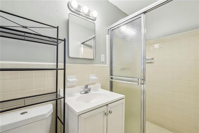 full bath featuring toilet, tile walls, vanity, a stall shower, and wainscoting