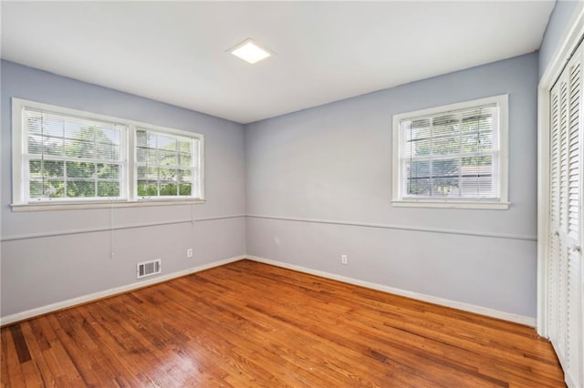 unfurnished room with plenty of natural light, visible vents, wood finished floors, and baseboards