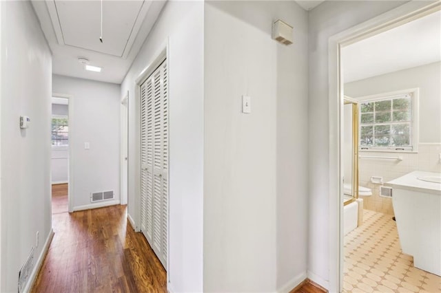 corridor featuring tile walls, attic access, visible vents, and wood finished floors