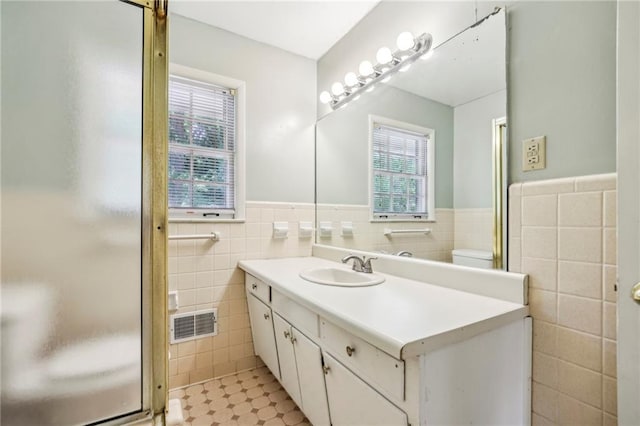 bathroom with tile walls, a wainscoted wall, vanity, visible vents, and a shower stall