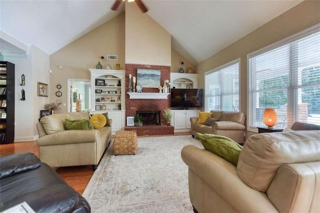 living room with high vaulted ceiling, ceiling fan, a brick fireplace, and hardwood / wood-style flooring