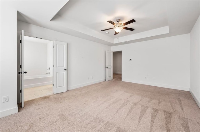 unfurnished room featuring light carpet, a tray ceiling, a ceiling fan, and baseboards