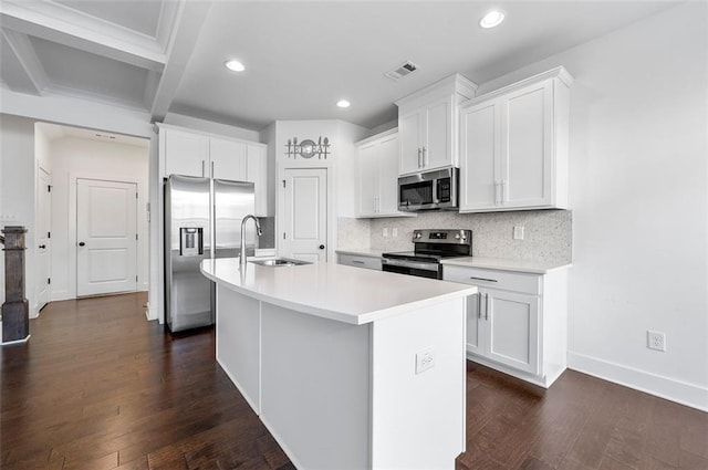 kitchen with stainless steel appliances, light countertops, white cabinets, a sink, and an island with sink