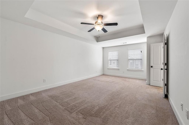 unfurnished room with light carpet, baseboards, a tray ceiling, and a ceiling fan