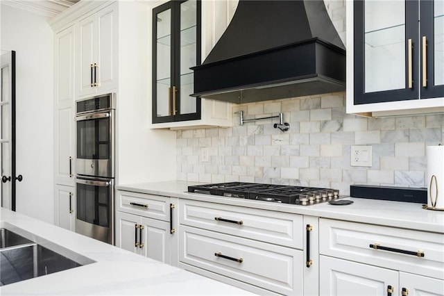 kitchen with premium range hood, backsplash, white cabinetry, and appliances with stainless steel finishes