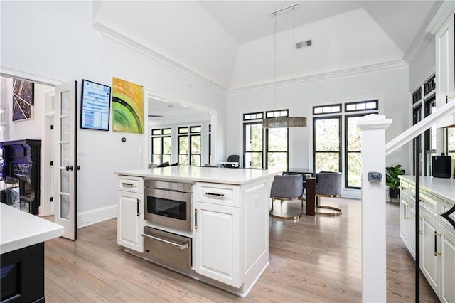 kitchen featuring french doors, light wood-type flooring, decorative light fixtures, a center island, and white cabinetry