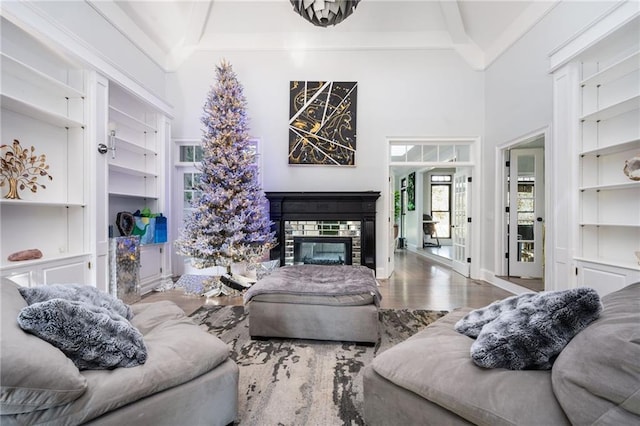 living room with a stone fireplace, built in features, beamed ceiling, and hardwood / wood-style flooring