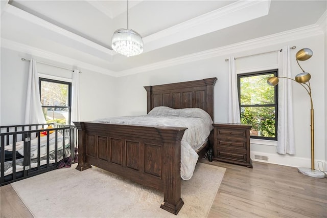 bedroom featuring a tray ceiling, multiple windows, light hardwood / wood-style flooring, and ornamental molding