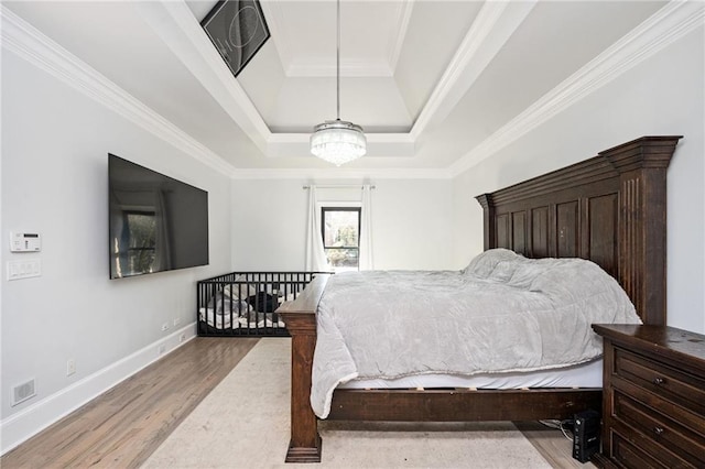 bedroom featuring light wood-type flooring, a raised ceiling, and ornamental molding