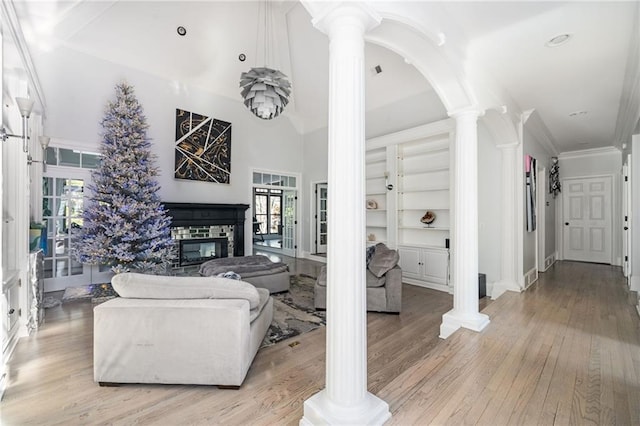 living room with ornate columns, built in features, crown molding, a fireplace, and light wood-type flooring