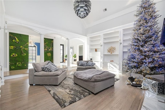 living room featuring hardwood / wood-style flooring, built in shelves, high vaulted ceiling, and decorative columns