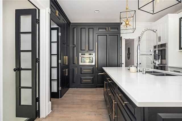 kitchen with sink, double oven, an island with sink, pendant lighting, and hardwood / wood-style flooring