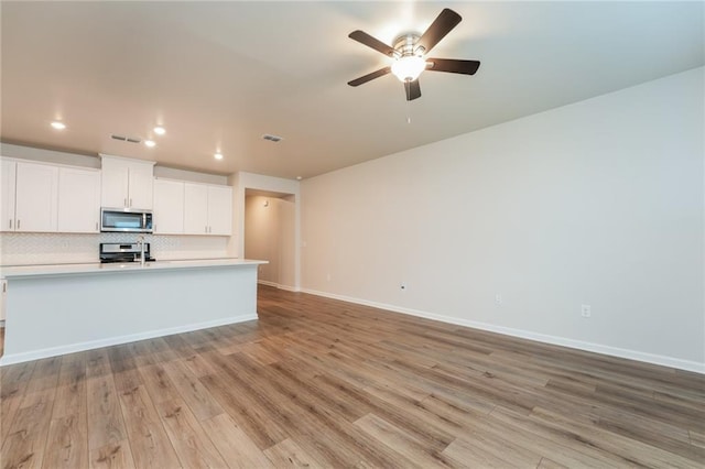 kitchen with ceiling fan, light wood-type flooring, white cabinetry, decorative backsplash, and stainless steel appliances