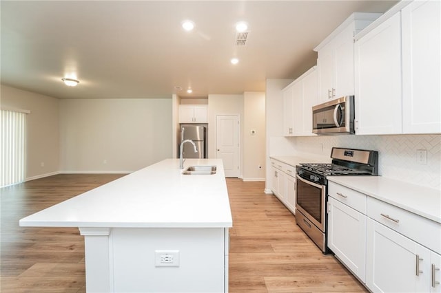 kitchen featuring appliances with stainless steel finishes, sink, backsplash, white cabinets, and a kitchen island with sink