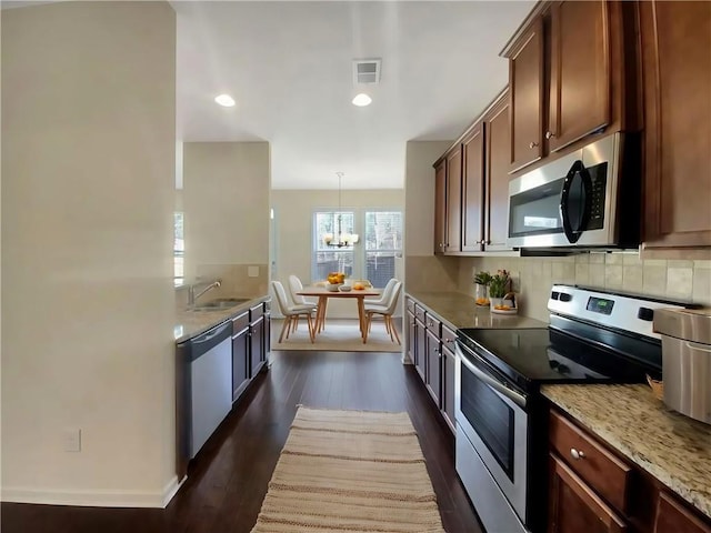 kitchen featuring sink, dark hardwood / wood-style floors, light stone countertops, decorative light fixtures, and stainless steel appliances