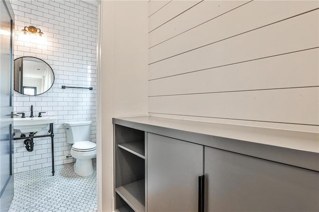 bathroom featuring a sink, tile walls, toilet, and tile patterned floors