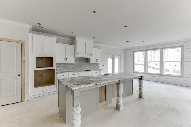 kitchen featuring a kitchen breakfast bar, light stone counters, crown molding, a center island, and white cabinetry