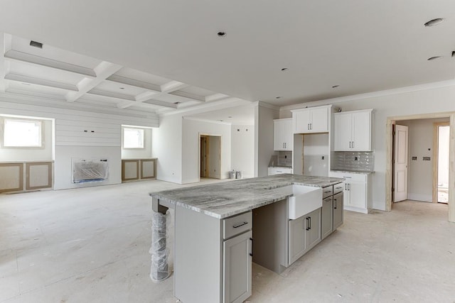 kitchen with light stone countertops, a center island, beamed ceiling, and coffered ceiling