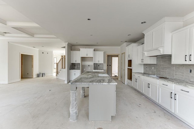 kitchen with white cabinets, a center island, light stone counters, and backsplash