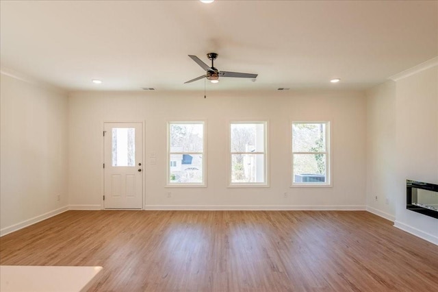 unfurnished living room with baseboards, a glass covered fireplace, visible vents, and light wood-style floors