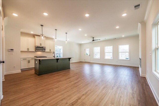 kitchen featuring a breakfast bar, visible vents, white cabinets, open floor plan, and stainless steel microwave