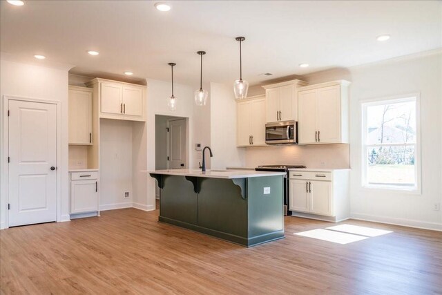 kitchen with light wood finished floors, stainless steel appliances, white cabinets, an island with sink, and a kitchen breakfast bar