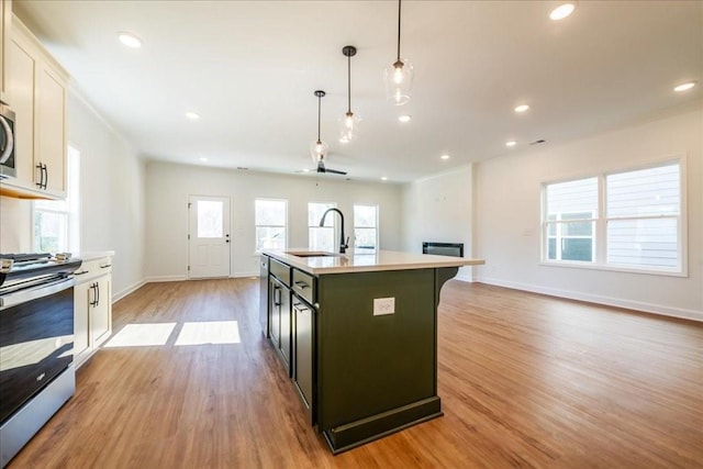 kitchen featuring a kitchen island with sink, stainless steel appliances, a sink, light countertops, and light wood finished floors