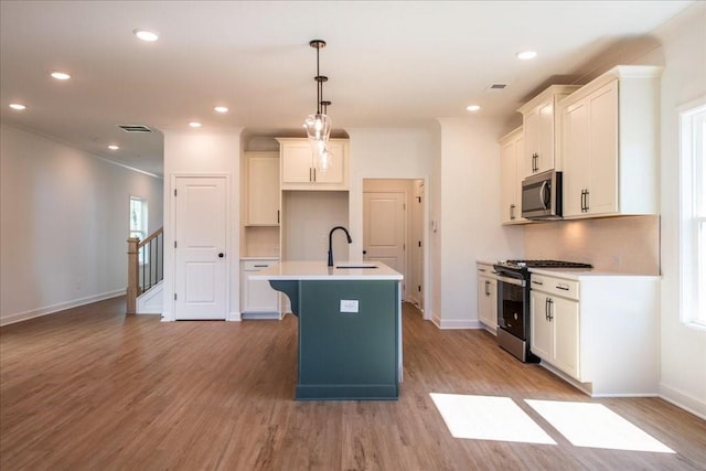 kitchen with light wood finished floors, a kitchen island with sink, visible vents, and stainless steel appliances