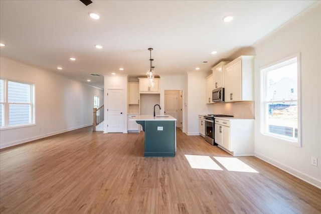 kitchen featuring appliances with stainless steel finishes, a kitchen island with sink, a sink, and light wood-style flooring