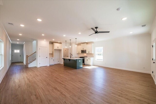 unfurnished living room featuring visible vents, stairway, light wood-style floors, a sink, and recessed lighting