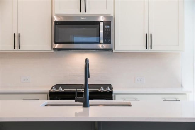 kitchen featuring light countertops, stainless steel microwave, backsplash, and white cabinetry