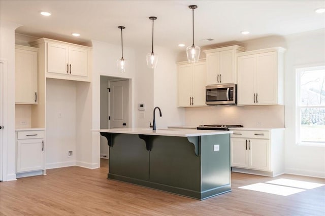 kitchen featuring light wood-type flooring, stainless steel microwave, a sink, and a center island with sink