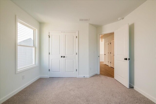 unfurnished bedroom featuring light carpet, a closet, visible vents, and baseboards