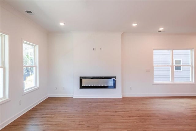 unfurnished living room featuring light wood finished floors, baseboards, visible vents, a glass covered fireplace, and ornamental molding