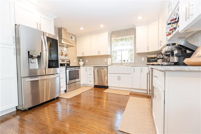 kitchen featuring appliances with stainless steel finishes, wall chimney range hood, white cabinetry, and decorative backsplash