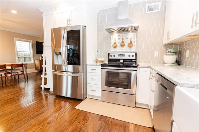 kitchen with stainless steel appliances, wood finished floors, visible vents, ornamental molding, and wall chimney range hood