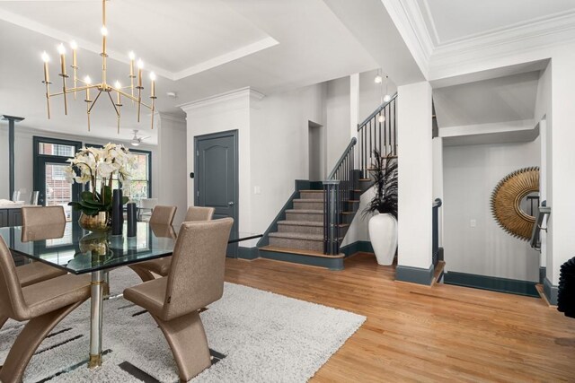 dining space featuring a raised ceiling, a notable chandelier, wood finished floors, and stairway