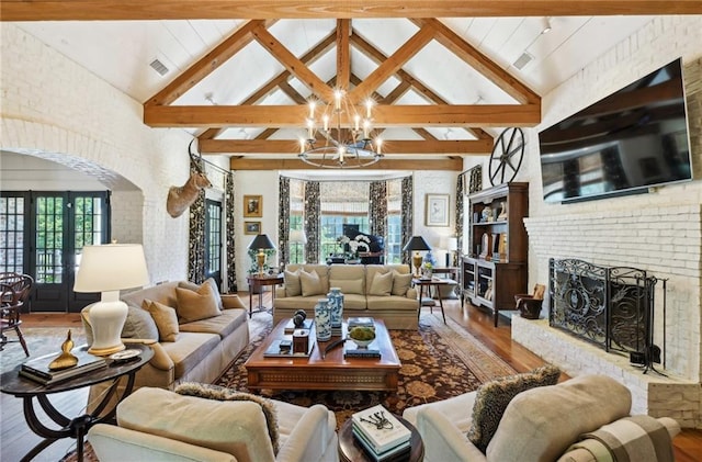 living room with a brick fireplace, beamed ceiling, hardwood / wood-style flooring, and a notable chandelier