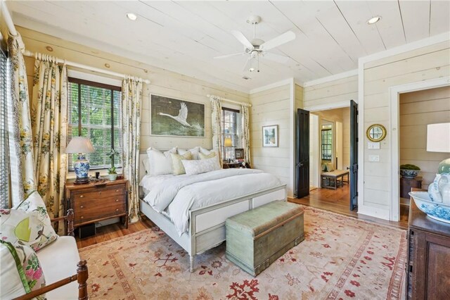 bedroom featuring multiple windows, wood walls, ceiling fan, and light hardwood / wood-style flooring