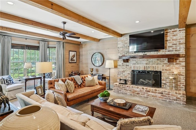 living room featuring a brick fireplace, beamed ceiling, wooden walls, and ceiling fan